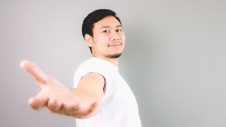 A man offering a help. An asian man with white t-shirt and grey background.の写真素材