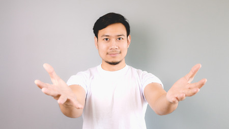 A man offering something. An asian man with white t-shirt and grey background.の写真素材