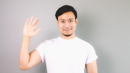 Show hand sign of hi and bye bye. An asian man with white t-shirt and grey background.の写真素材