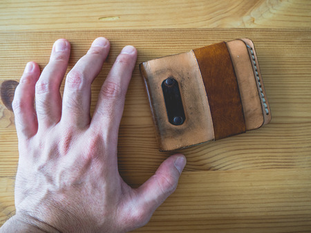 Grunged and dirty leather wallet on wooden table. Hand grab leather wallet.