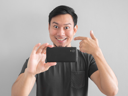 Funny Asian man taking photo with smartphone. Black t-shirt mourn for Thai king.の写真素材