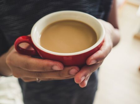 Woman hold red cup of  coffee in hand in soft morning light.の写真素材