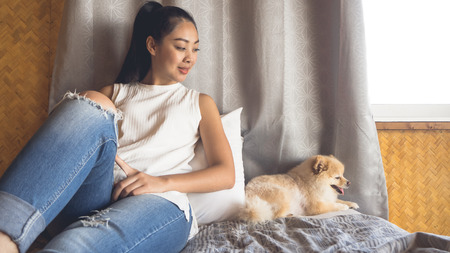 Asian woman relax on bed with her dog in bamboo bedroom.の写真素材