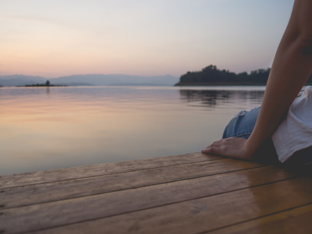 Woman resting her legs by the beautiful lake in sunset scene.の写真素材