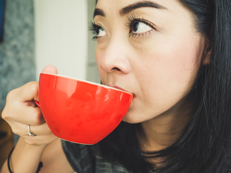 Asian woman drinks morning coffee in red cup in her bedroom. Thai Japanese chinese and Indonesian.の写真素材