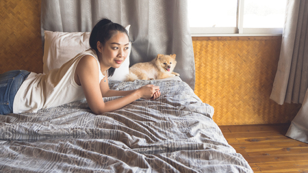 Asian woman relax on bed with her dog in bamboo bedroom.の写真素材