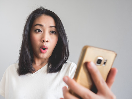 Surprise and shock face of Asian woman look at the smartphone in her hand.の写真素材