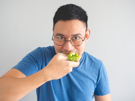 Asian man eat sandwich with vegetable and egg and make funny face.の写真素材