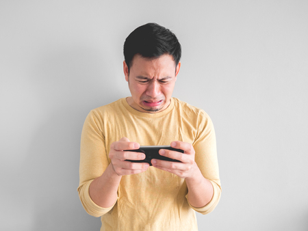 Crying Asian man is losing the mobile game in his smartphone.の写真素材