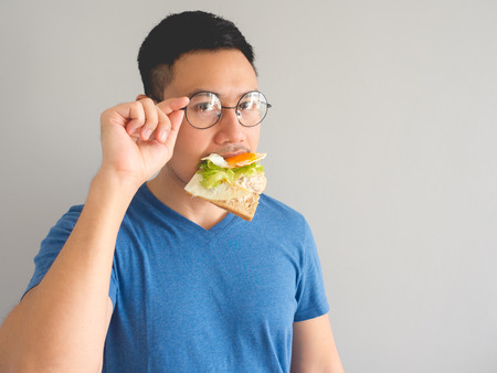 Asian man eat sandwich with vegetable and egg and make funny face.の写真素材