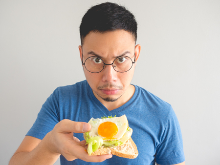 Asian man eat sandwich with vegetable and egg and make funny face.の写真素材