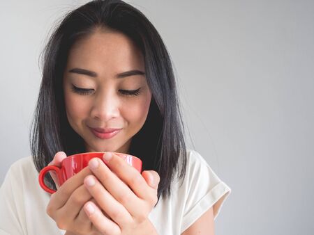 Smile Asian woman is drinking coffee from red cup.の写真素材