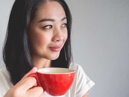 Smile Asian woman is drinking coffee from red cup.の写真素材