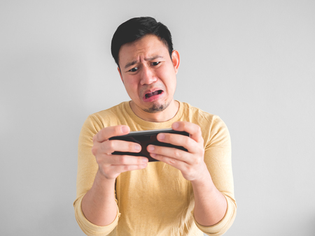 Crying Asian man is losing the mobile game in his smartphone.の写真素材