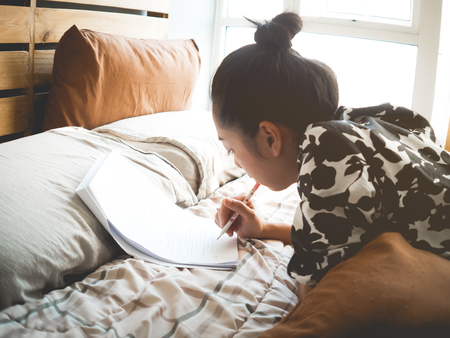 Asian woman reads book for exam on her bed in bedroom morning.の写真素材