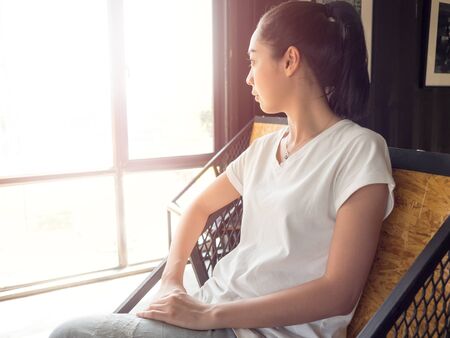 Asian woman rest on chair in the coffee cafe and looking out to the sun by the windows.の写真素材