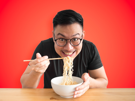 Happy Asian man eats instant noodles with big smile isolated on colour background.の写真素材