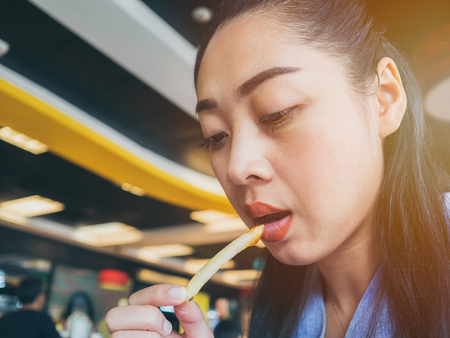 Asian woman is eating french fries in fastfood restuarant.の写真素材