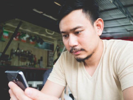 Asian man using mobile phone in an outdoor cafe.の写真素材
