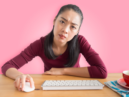 Unstatisfied and serious Asian woman working on her office desk with coffee mouse and keyboard.の写真素材