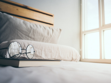Concept of reading and relax. Eyeglasses and black book on wooden loft bed in bedroom.の写真素材