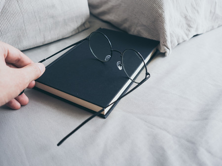 Concept of reading and relax. Eyeglasses and black book on wooden loft bed in bedroom.の写真素材