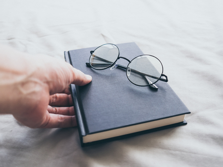 Concept of reading and relax. Eyeglasses and black book on wooden loft bed in bedroom.の写真素材