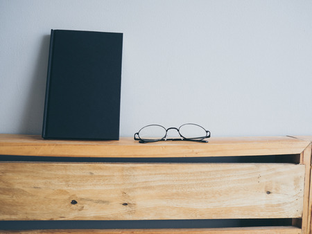 Concept of reading and relax. Eyeglasses and black book on wooden loft bed in bedroom.