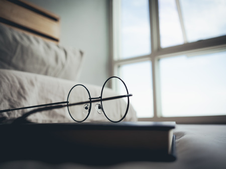 Concept of reading and relax. Eyeglasses and black book on wooden loft bed in bedroom.の写真素材