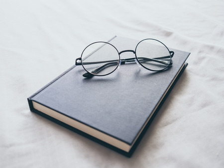 Concept of reading and relax. Eyeglasses and black book on wooden loft bed in bedroom.