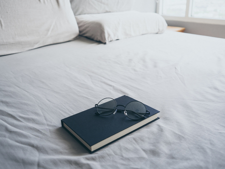 Concept of reading and relax. Eyeglasses and black book on wooden loft bed in bedroom.の写真素材