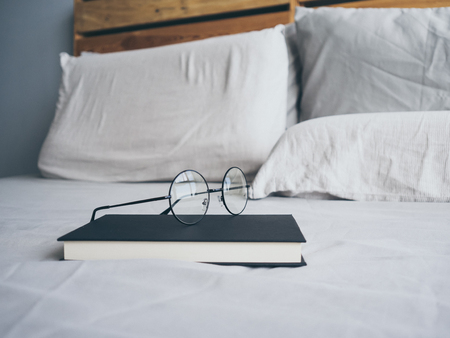 Concept of reading and relax. Eyeglasses and black book on wooden loft bed in bedroom.