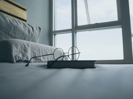 Concept of reading and relax. Eyeglasses and black book on wooden loft bed in bedroom.の写真素材