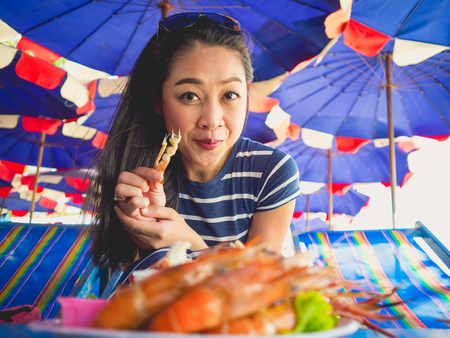 Close up of Asian woman eating local grilled seafood of Thailand beach.の写真素材