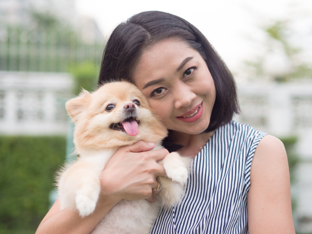 Asian woman plays with her pomeranian puppy in the garden.の写真素材