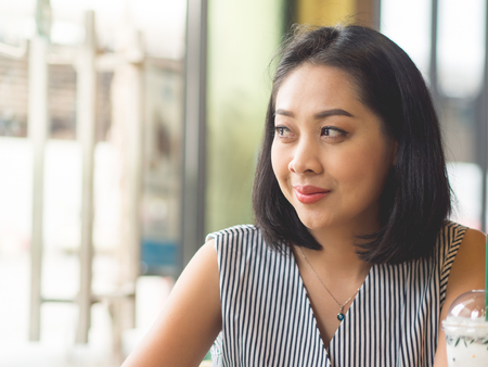 Asian woman sits in coffee cafe wirh iced coffee on table.の写真素材