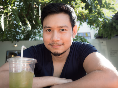 Asian man drinking iced green tea at the garden of the cafe.