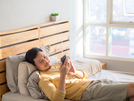 Asian man using smartphone in his bed in the morning.の写真素材