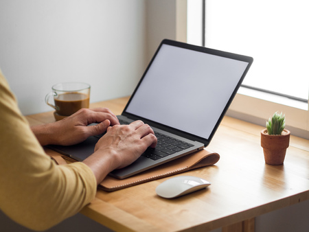 Man using laptop on a desk with coffee in morning light.