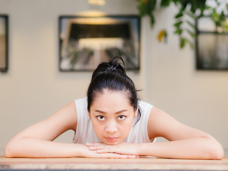 Asian woman with bored expression is waiting for some one or thinking of something.