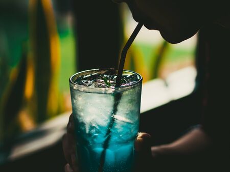 Woman is drinking a glass of Iced Blue Lemon Soda with low light from window.