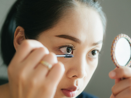 Asian woman is putting make up mascara on her eyelashes.の写真素材