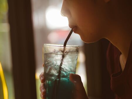 Woman is drinking a glass of Iced Blue Lemon Soda with low light from window.