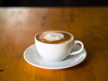 Hot coffee latte art in white cup on wooden table.の写真素材