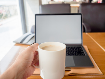 Laptop with white empty screen display on wooden table with a mug of coffee. Concept of working in co-working space.の写真素材