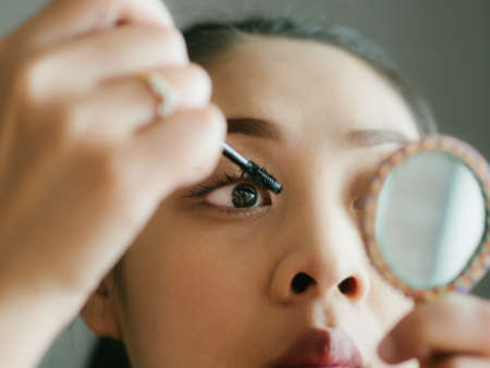 Asian woman is putting make up mascara on her eyelashes.