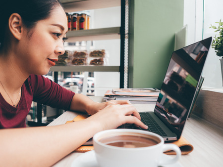 Asian woman is using laptop with a cup of hot coffee in the cafe.の写真素材