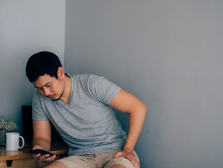 Asian man is using smartphone in his home office.