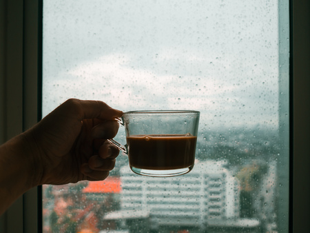 Hand holding a glass of hot coffee on rain drops windows.の写真素材