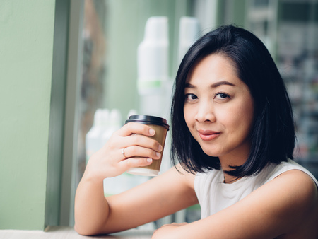Happy Asian woman is drinking hot cup of coffee in peaceful atmosphere.の写真素材